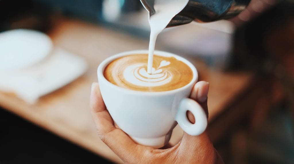 a photo of a barista pouring a latte with a delicate leaf design in the center of the cup.